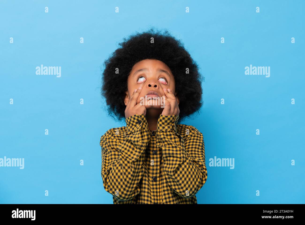 Afro-afrikanischer Junge, der lustiges Gespenstergesicht in hellblauem isoliertem Hintergrundstudio macht Stockfoto