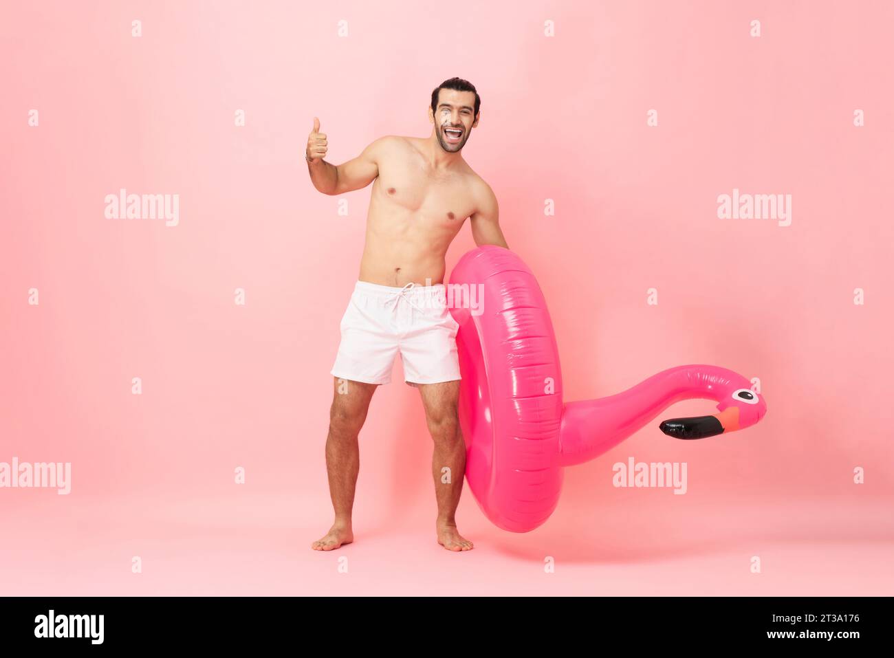 Ganzkörper-Sommerporträt eines glücklichen kaukasischen Mannes, der die Daumen hochgibt und Gummiring in rosa Farbe hält, isolierte Hintergrundaufnahme im Studio Stockfoto