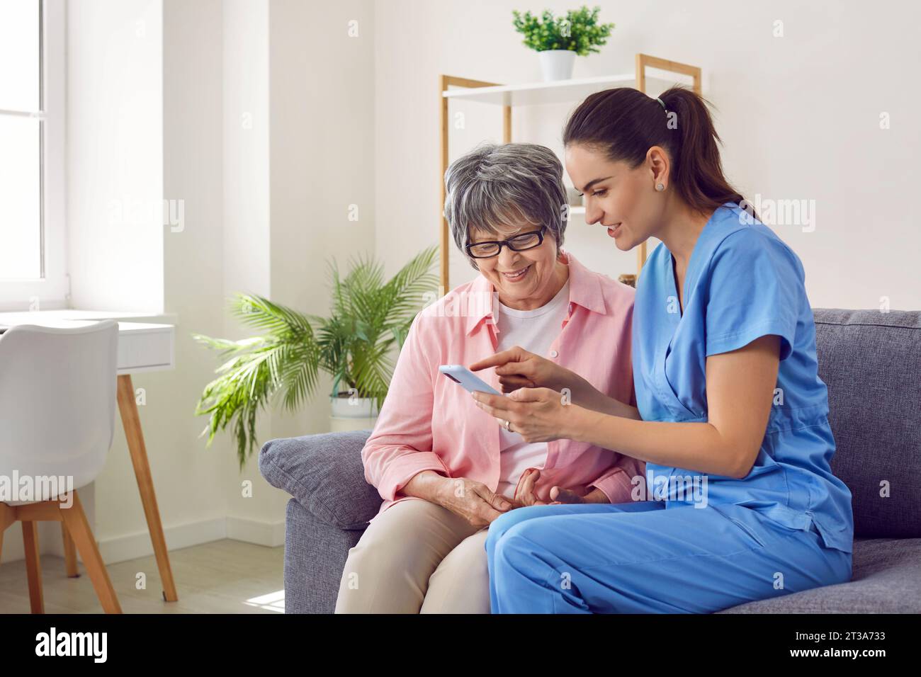 Demenz im Alter. Eine junge hübsche Krankenschwester zu Hause zeigt einer älteren Frau ein Foto auf einem Handy. Stockfoto