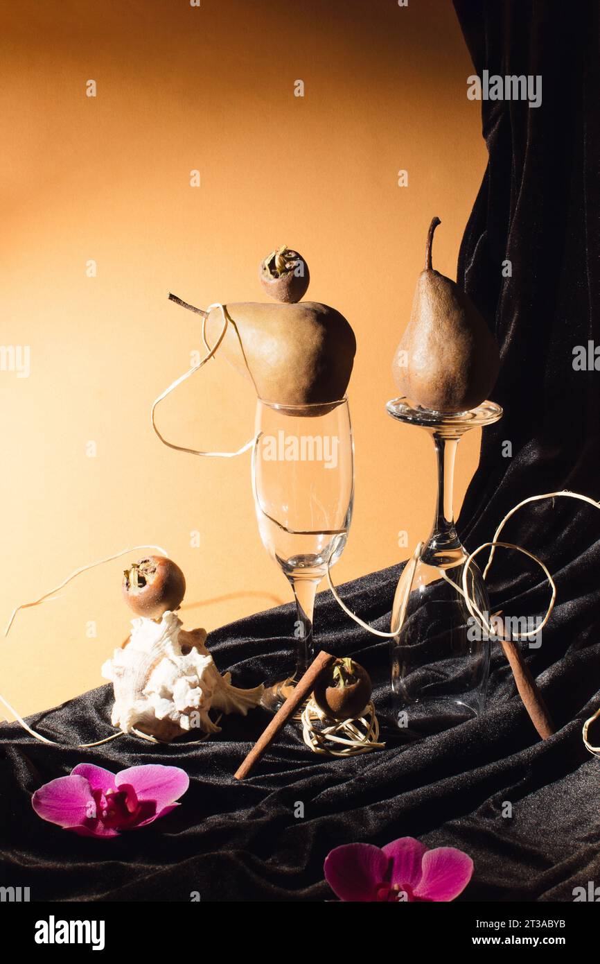 Künstlerisches Stillleben mit Birnen, Muscheln, Weingläsern und Medlar in Kombination mit Orchideenblüten. Kreatives Poster- und Hintergrundbild-Konzept Stockfoto