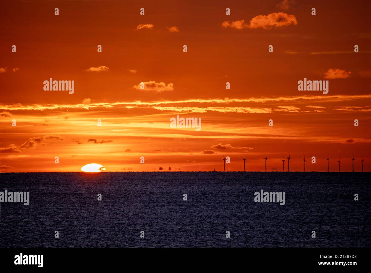 Die Sonne taucht am Horizont über dem Englischen Kanal vorbei mit Rampion Wind Farm Turbines vor feurigem Himmel. Stockfoto