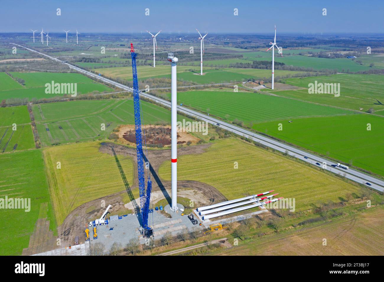 Aus der Vogelperspektive über die Baustelle mit Rotorblättern auf dem Boden und Baukran zur Montage von Stahlturmabschnitten der Windkraftanlage im Windpark Stockfoto