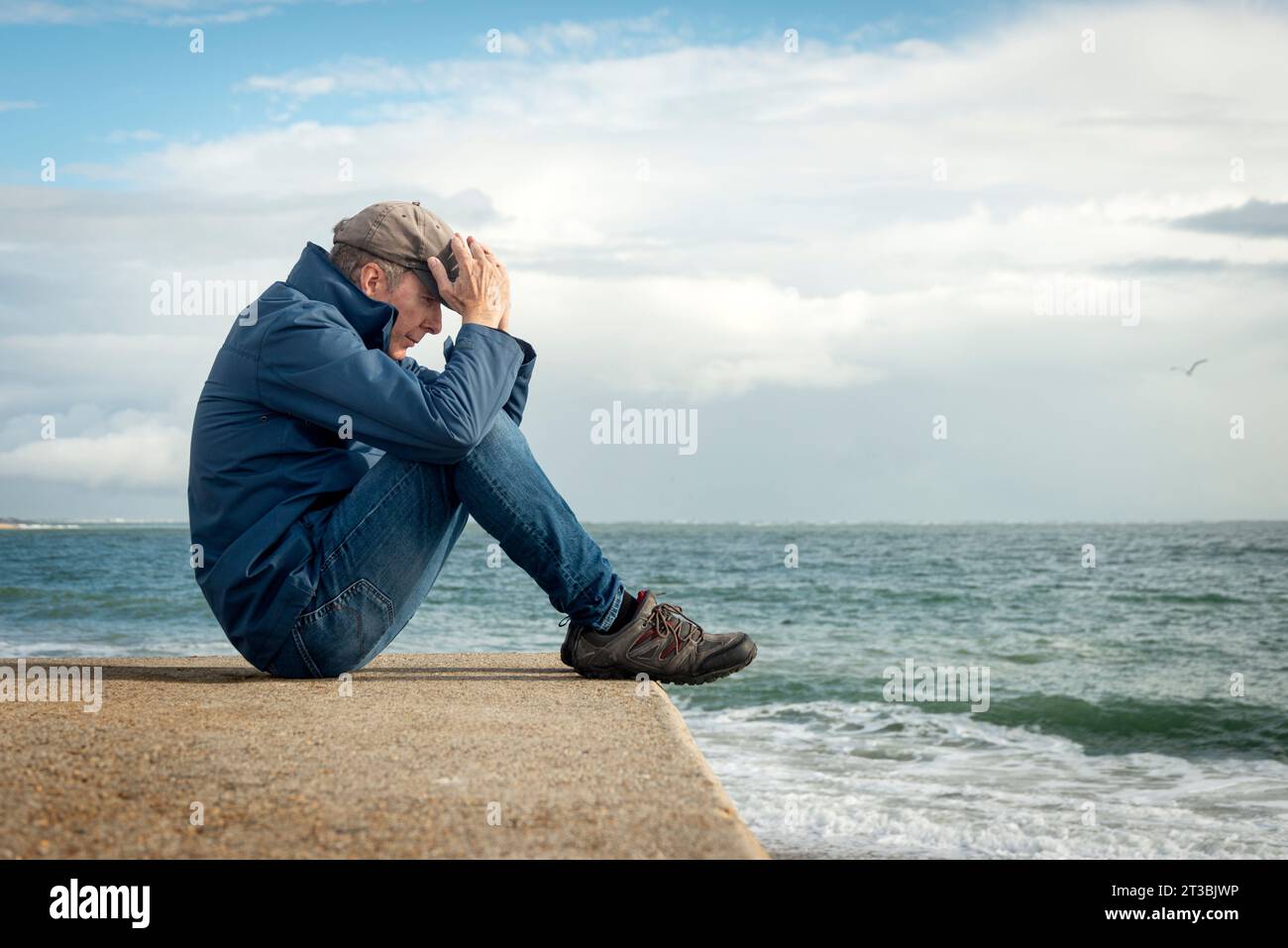 Mann, der am Meer sitzt, mit dem Kopf in den Händen, Emotionen, geistiges Gesundheitskonzept Stockfoto