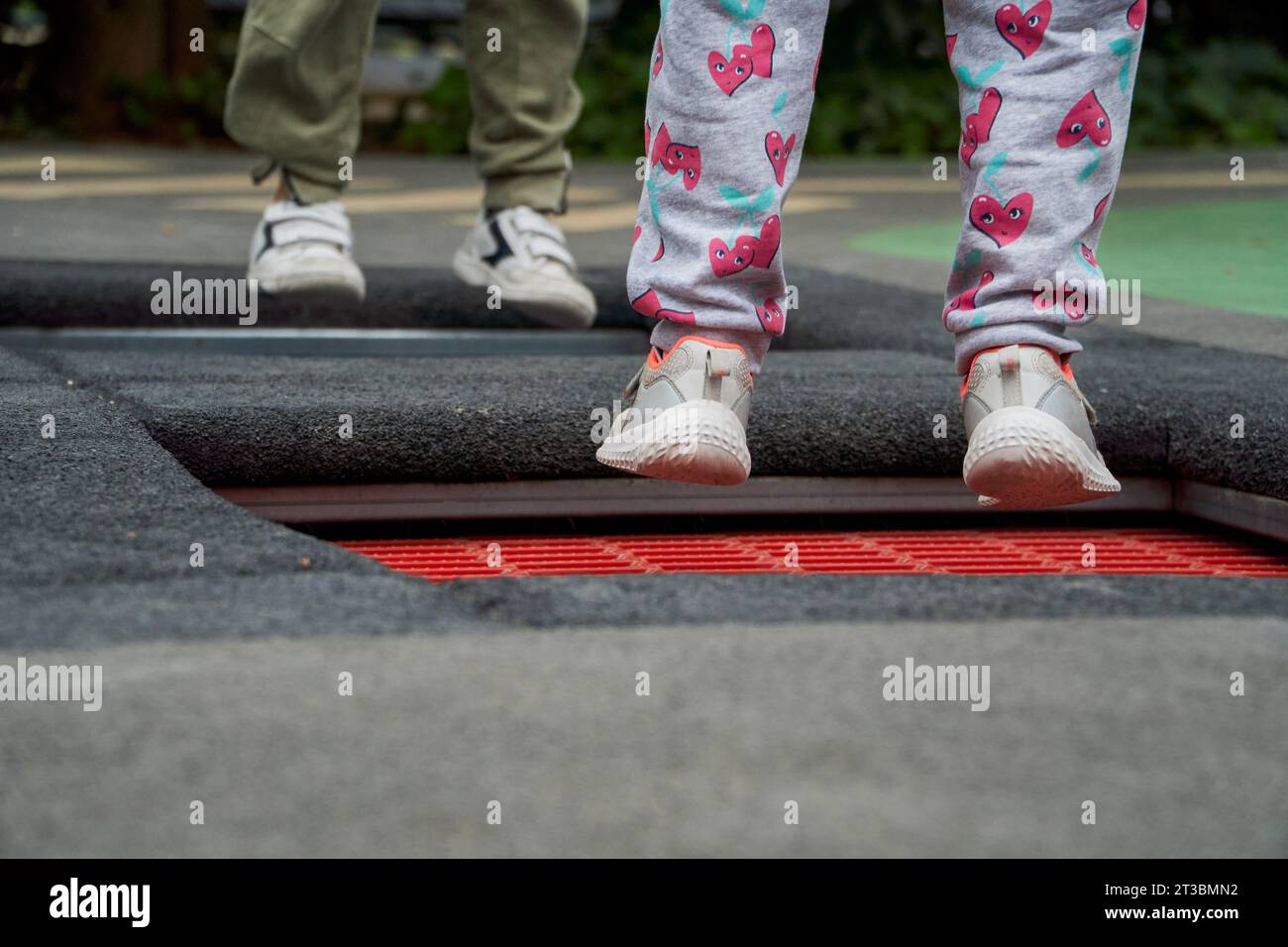 Nahaufnahme von Kinderfüßen, die zusammen auf dem Trampolin auf dem Parkboden springen Stockfoto