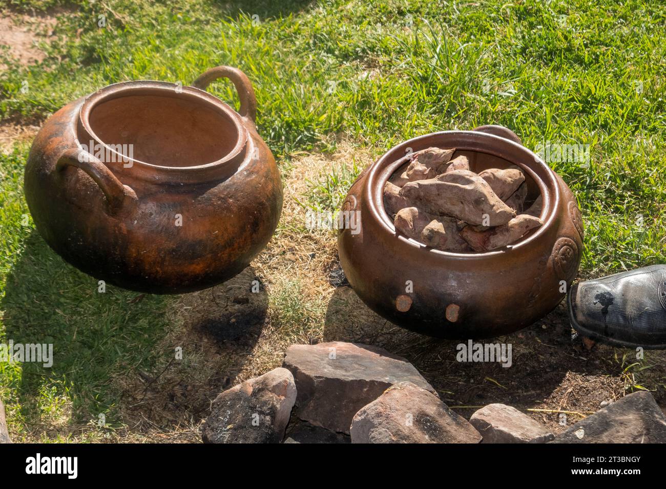 Steingut-Gerichte zum Kochen von Süßkartoffeln über Glut, die in einem Loch vergraben und mit heißen Steinen bedeckt sind. Stockfoto