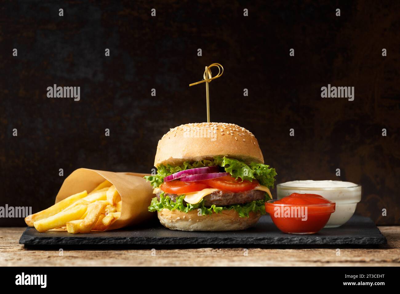 Burger mit Rinderschnitzel, Pommes frites, Saucen auf schwarzem Steinteller auf dunklem Hintergrund. Fast Food, Hamburger Stockfoto