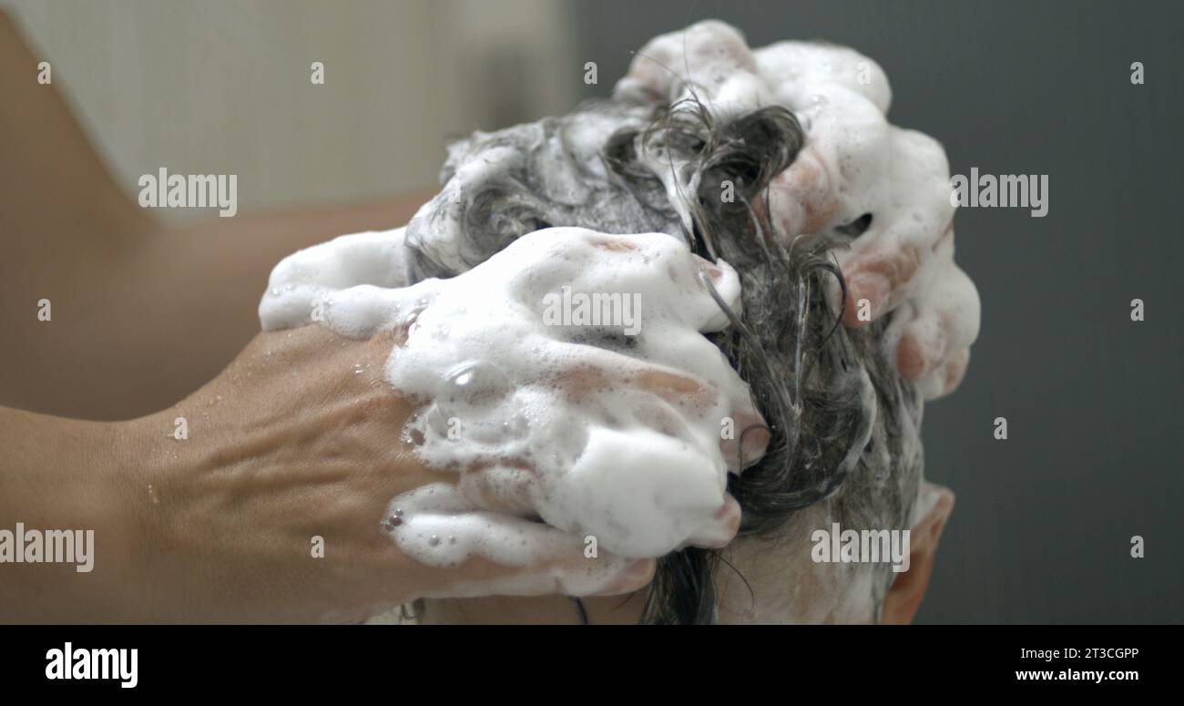 Elternhand wascht Kinderhaare mit Shampoo in Zeitlupe 800 fps. Junge schrubbt den Kinderkopf Stockfoto