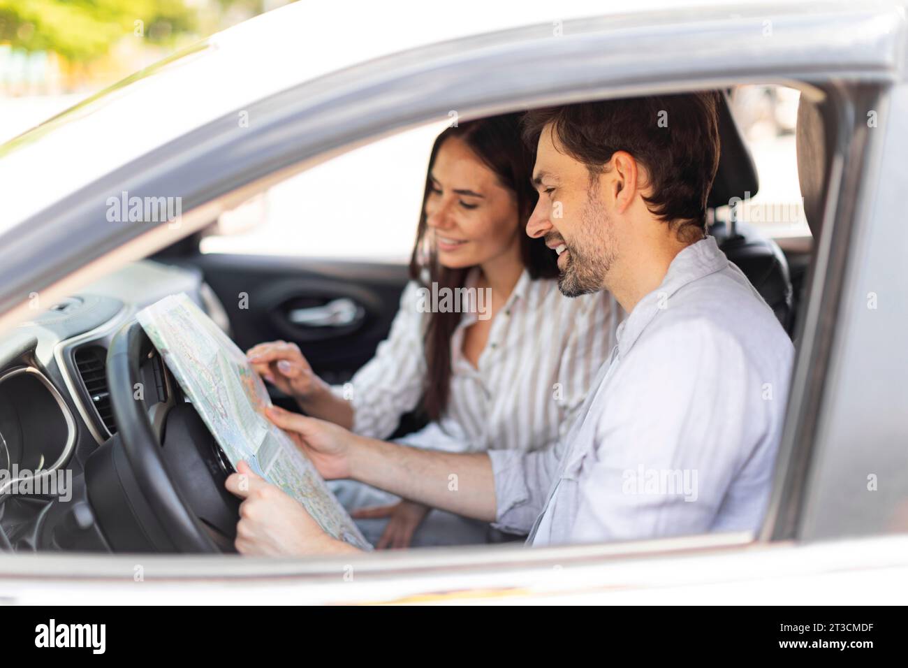 Ein lächelndes Paar, das sich die Karte auf Papier ansieht, sitzt im Auto Stockfoto
