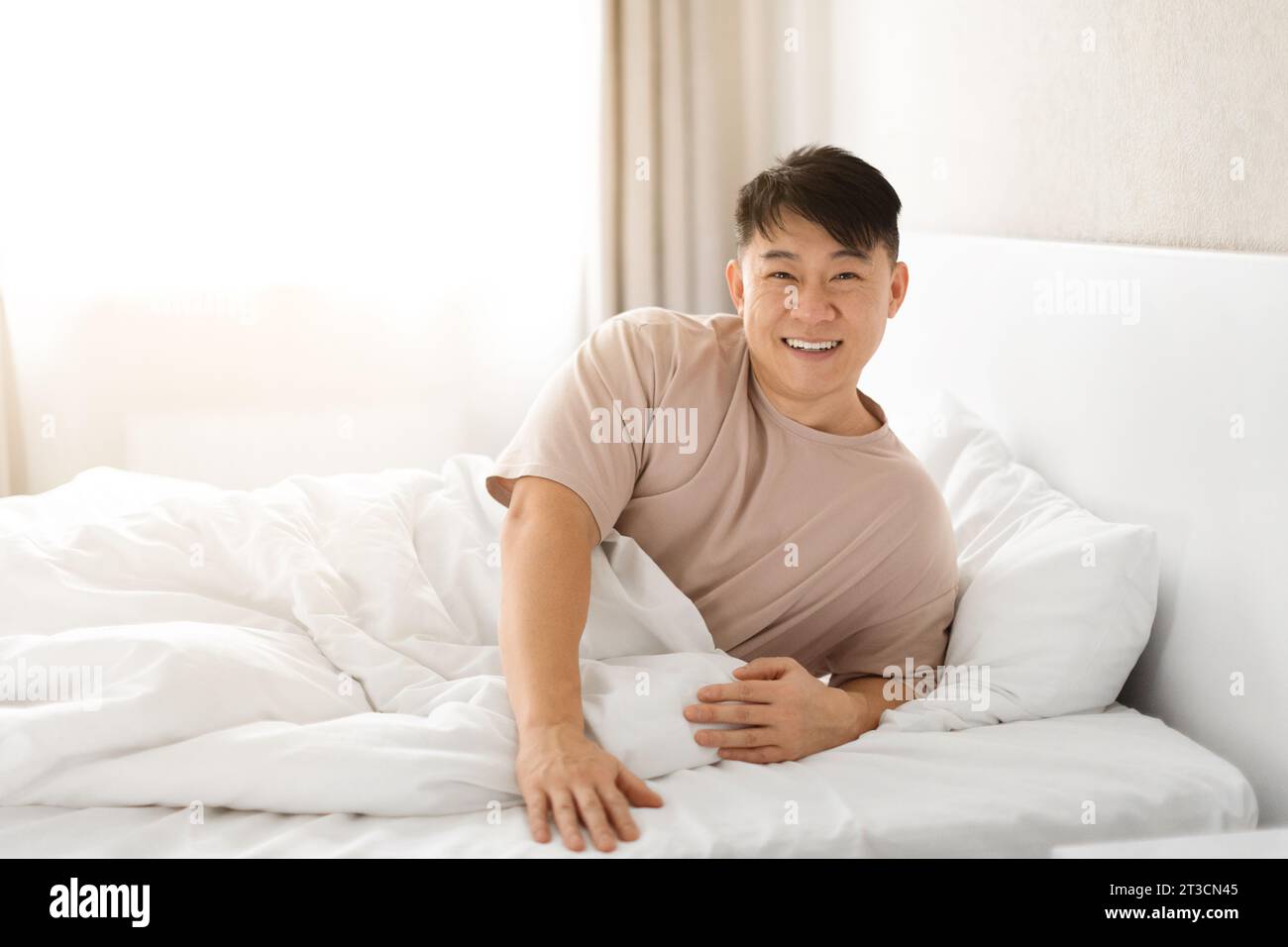 Ein glücklicher reifer asiatischer Mann wacht auf, sitzt auf dem Bett Stockfoto