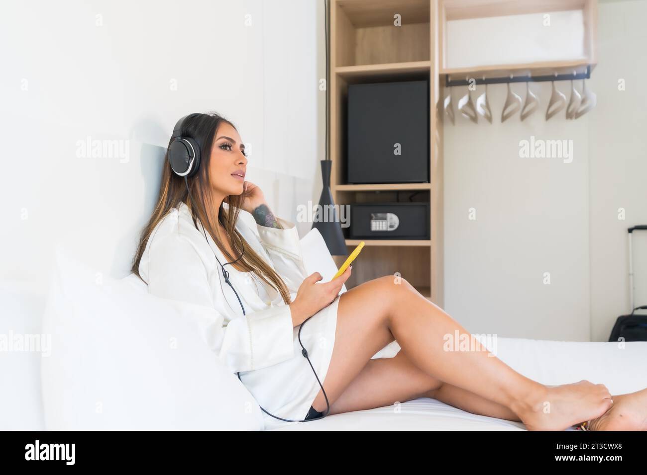 Schönheitsfrau in bequemer Kleidung, die Musik hört, die auf einem Hotelzimmer liegt Stockfoto