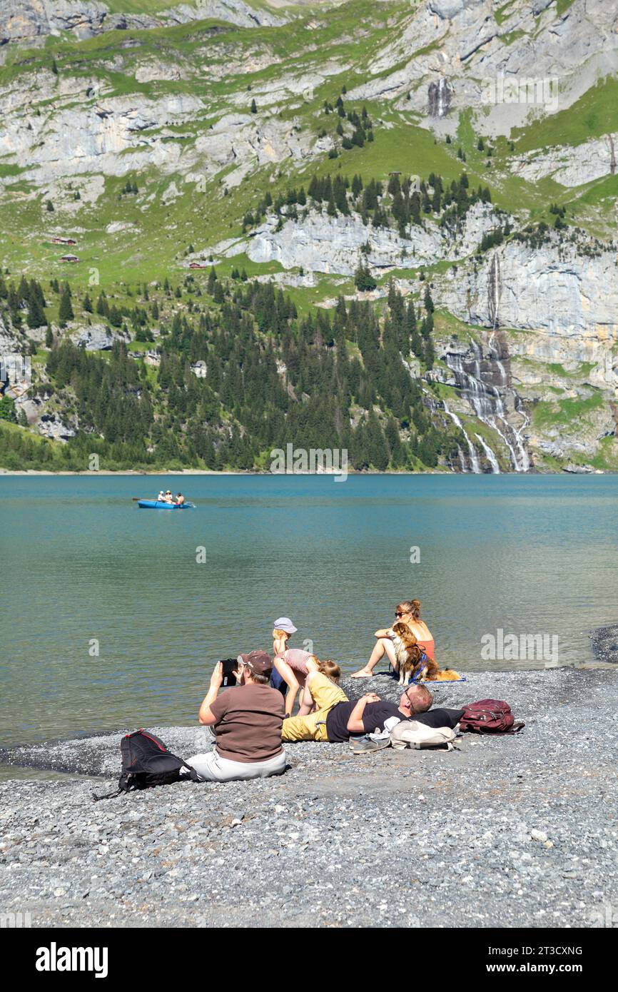 Oeschinensee, Schweiz–Aug 3,2023: Gruppe von Menschen genießt Sonnenschein neben einem blauen See im Alpenberg mit Felsenberg im Hintergrund Stockfoto