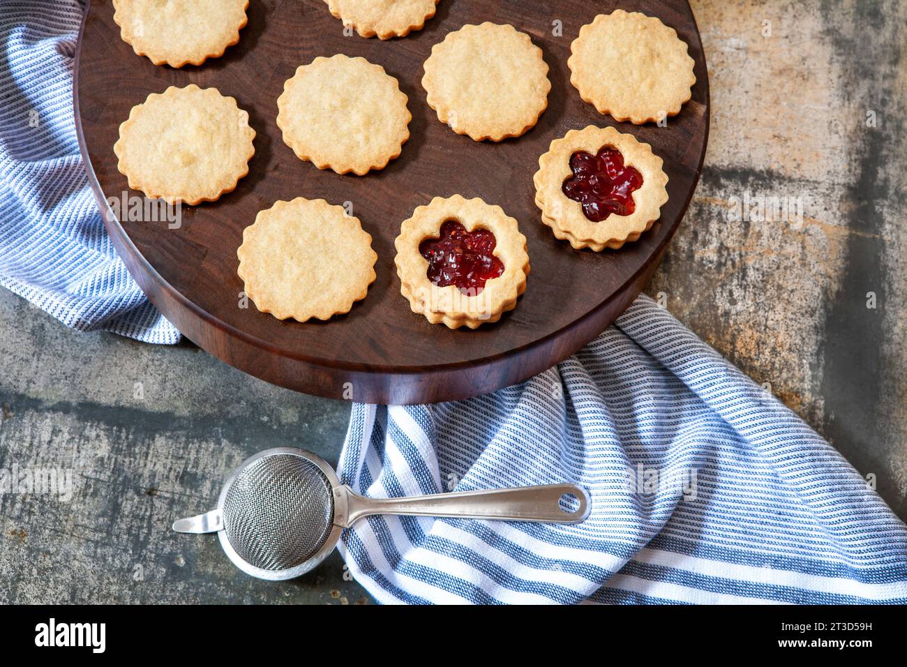 Hochwinkelansicht der Linzer Torten, die auf rundem Holzbrett mit blauem Handtuch und Mesh-Sieb montiert werden Stockfoto