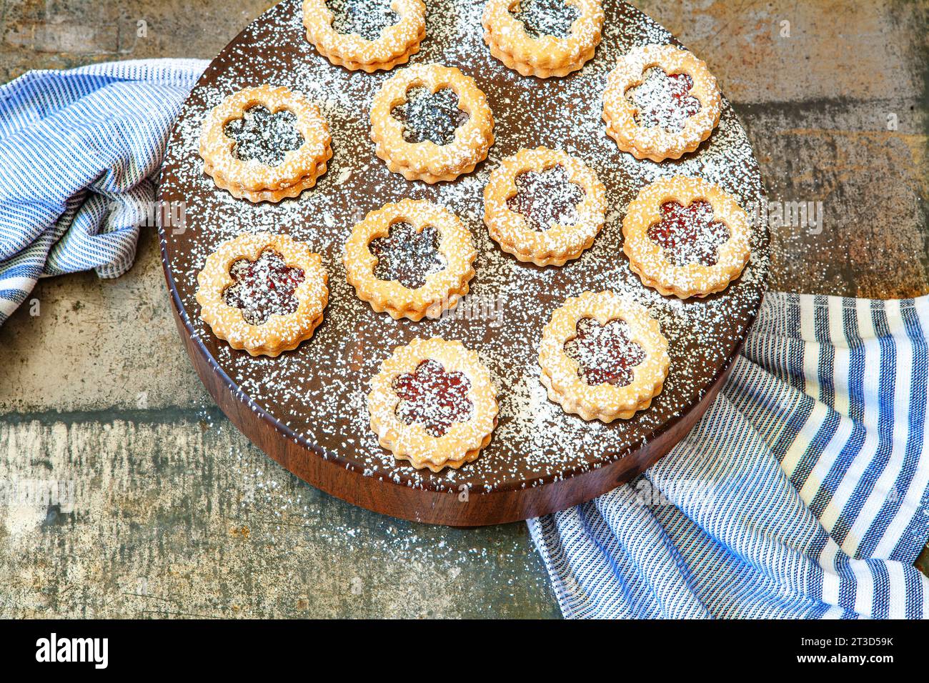 Hochwinkelansicht der mit Puderzucker bestäubten Linzer Torten auf rundem Holzbrett mit blauem Handtuch Stockfoto