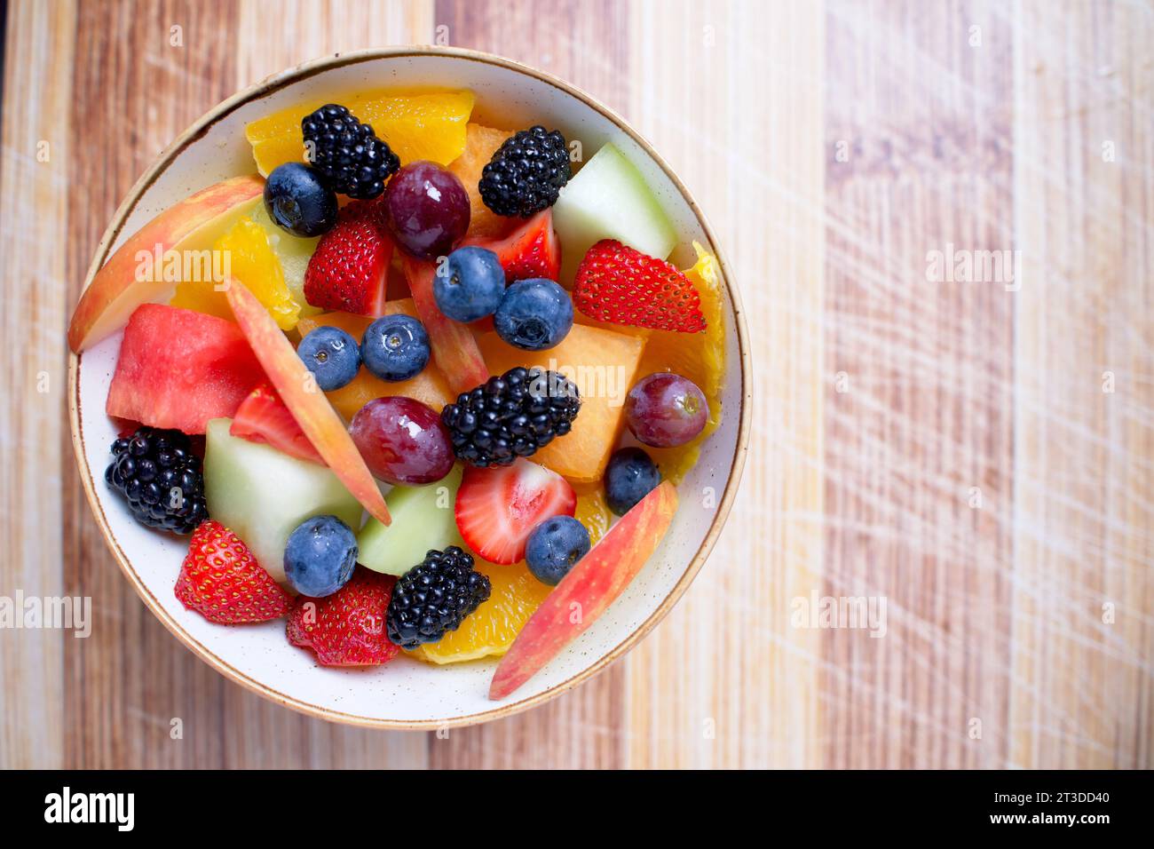 Schüssel mit frisch geschnittenem Obst auf einem hölzernen Schneidebrett mit Sonnenlicht nach rechts Stockfoto