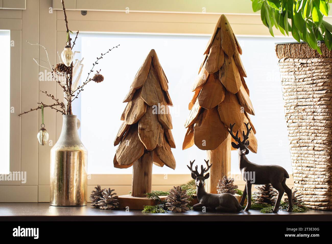 Weihnachtsdekoration. Künstliche Weihnachtsbäume aus Holz, Tannenzapfen und Hirschfiguren am Fenster im Inneren. Frohe Weihnachten Stockfoto