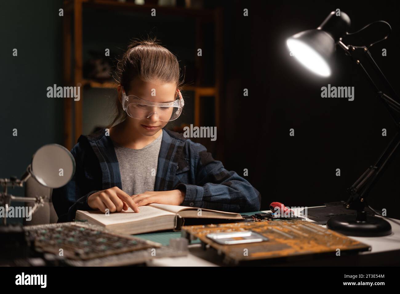 Teenager Mädchen zur freien Verfügung am Schreibtisch lernt Löten, Mädchen hat eine Schutzbrille, liest Bücher und repariert Kabel, Elektronik Stockfoto