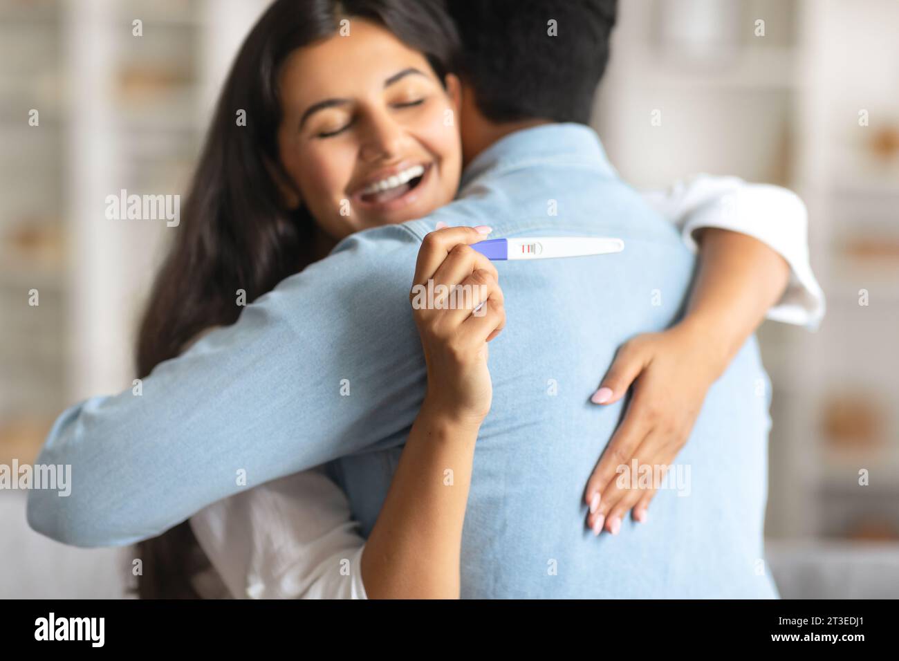 Indianerin umarmt freudig den Mann und hält einen positiven Schwangerschaftstest Stockfoto