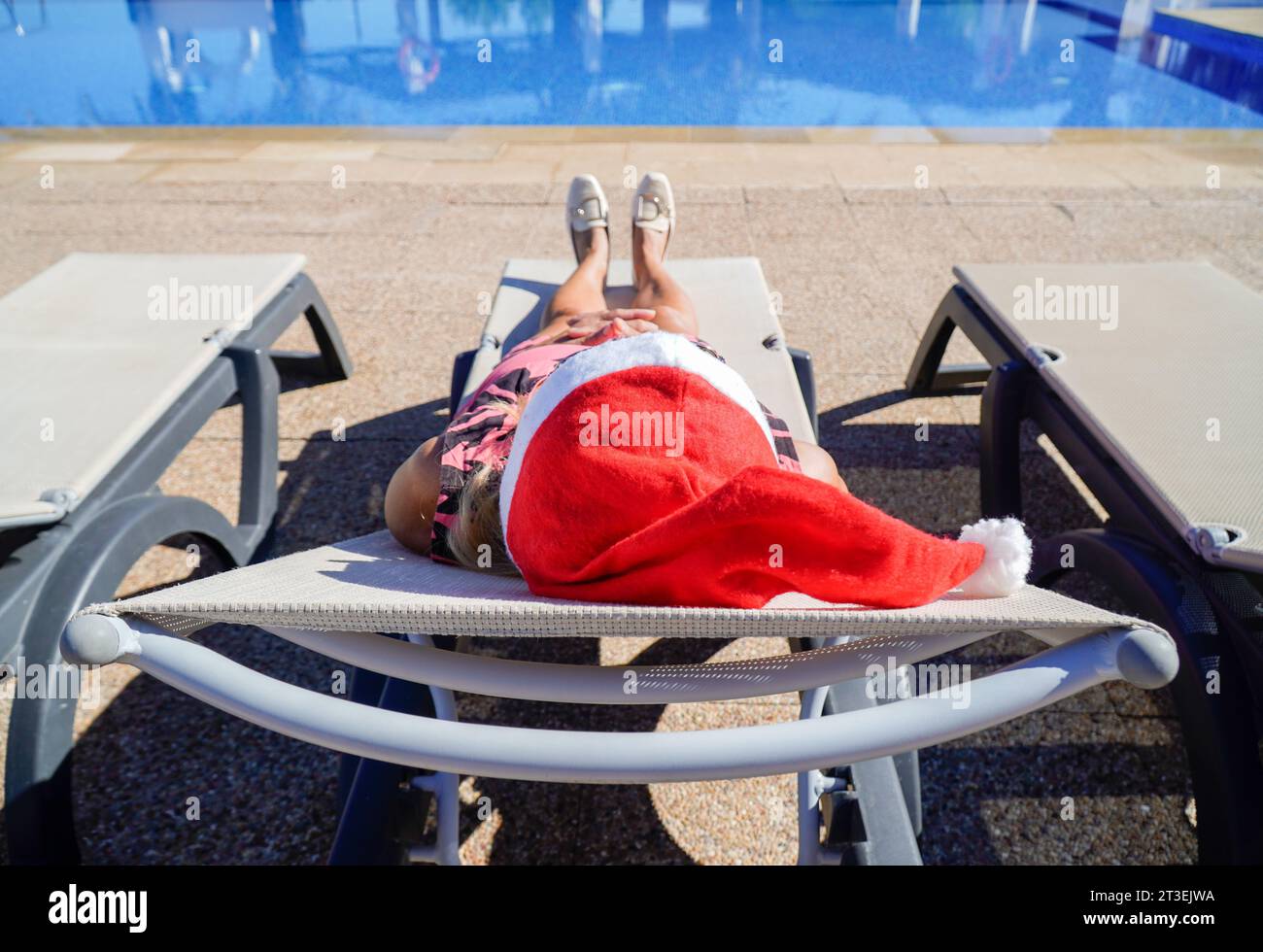 Reife Frau mit weihnachtsmütze, die in Weihnachten in einer Strandliege liegt. Weihnachten im Sommer Stockfoto