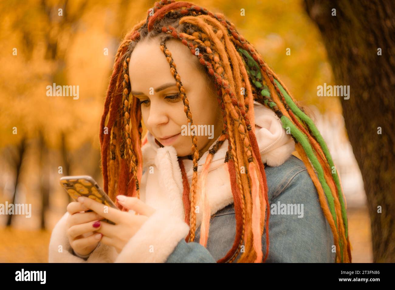 Schöne junge Frau mit Dreadlocks mit Smartphone im Herbstpark. Stockfoto