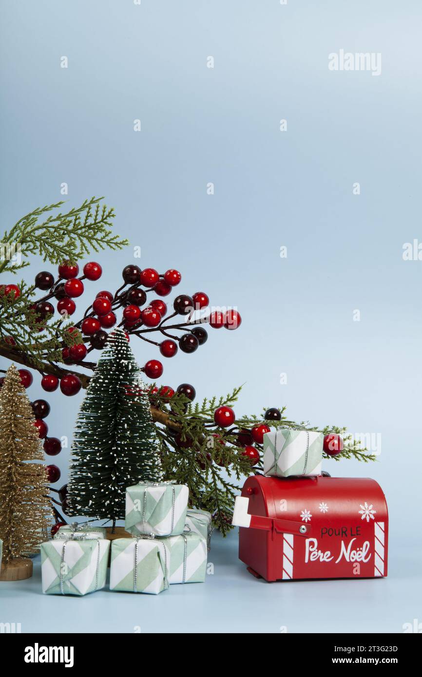 Komposition mit vielen Geschenken, einem Zweig der stechpalme mit seinen roten Beeren, einem Briefkasten des weihnachtsmanns und einem weihnachtsbaum vor einem leuchtenden himmelblauen Hintergrund. Stockfoto