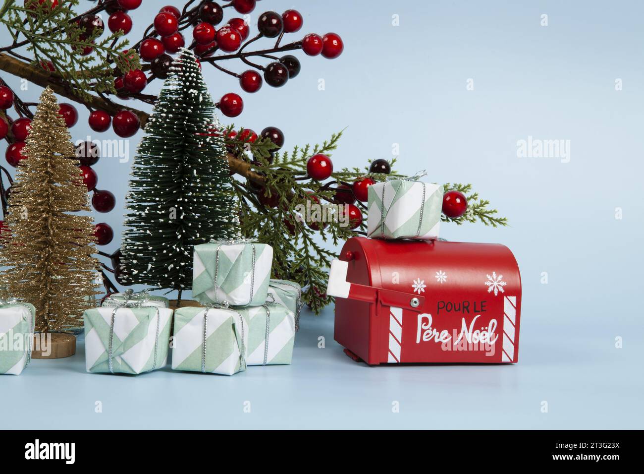 Komposition mit vielen Geschenken, einem Zweig der stechpalme mit seinen roten Beeren, einem Briefkasten des weihnachtsmanns und einem weihnachtsbaum vor einem leuchtenden himmelblauen Hintergrund. Stockfoto
