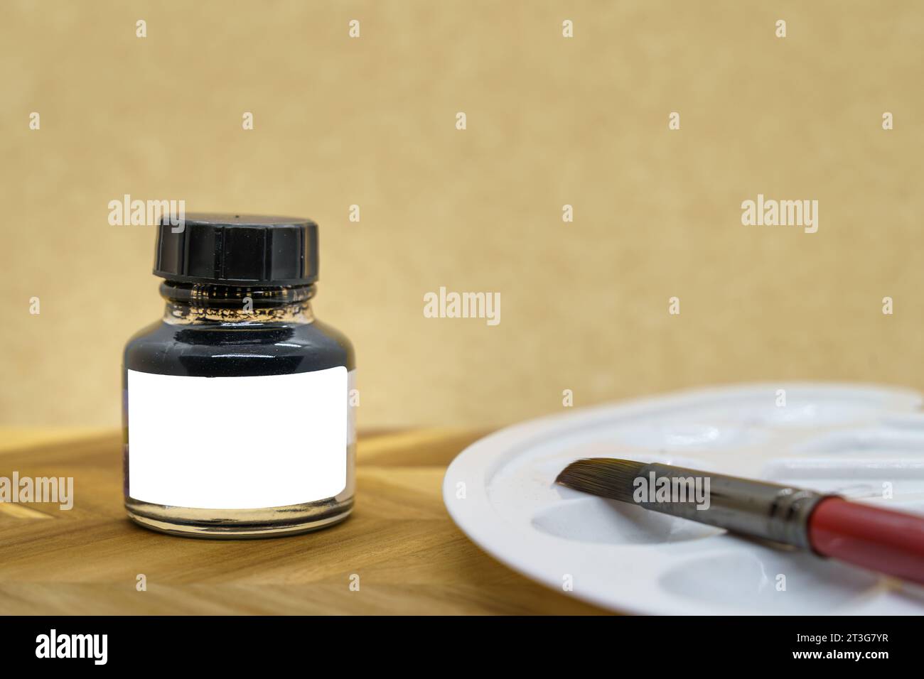 Schwarze Tintenflasche mit leerem weißem Etikett mit Pinsel und Palette, gelber Hintergrund, Modell. Stockfoto