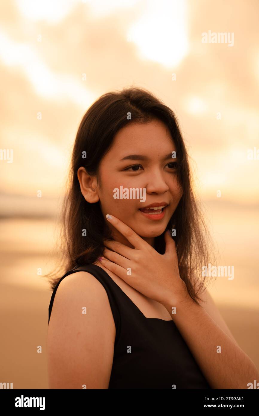 Eine asiatische Teenagerin mit schwarzem Hemd und schwarzem Haar hat ein süßes Gesicht, wenn sie lächelt und die Aussicht vor Sonnenaufgang genießt Stockfoto