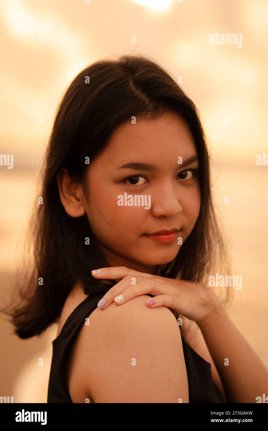 Eine asiatische Teenagerin mit schwarzem Hemd und schwarzem Haar hat ein süßes Gesicht, wenn sie lächelt und die Aussicht vor Sonnenaufgang genießt Stockfoto