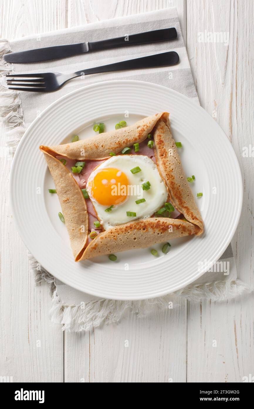 Hausgemachtes Buchweizen-Kreppegalette mit Ei, Schinken und grüner Zwiebelnaht auf dem Teller auf dem Tisch. Vertikale Draufsicht von oben Stockfoto