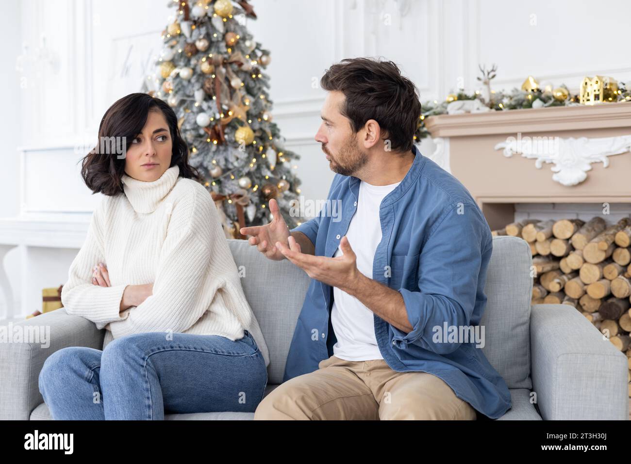 Junge Paare, Frau und Mann sitzen zu Hause auf dem Sofa an Silvester- und Weihnachtsfeiertagen und streiten sich. Ein Mann schreit seine Frau an, psychische Gewalt, Missbrauch. Stockfoto