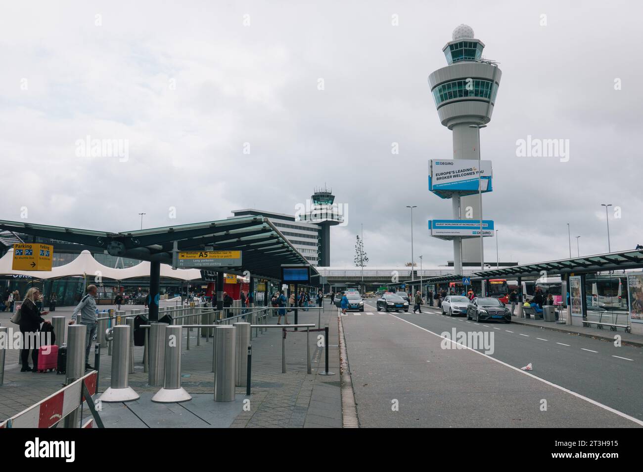 Der Kontrollturm am Flughafen Amsterdam Schiphol, von der Ankunftshalle aus gesehen, an einem bewölkten Tag. Eine DEGIRO-Anzeige ist auf einer Plakatwand zu sehen. Stockfoto