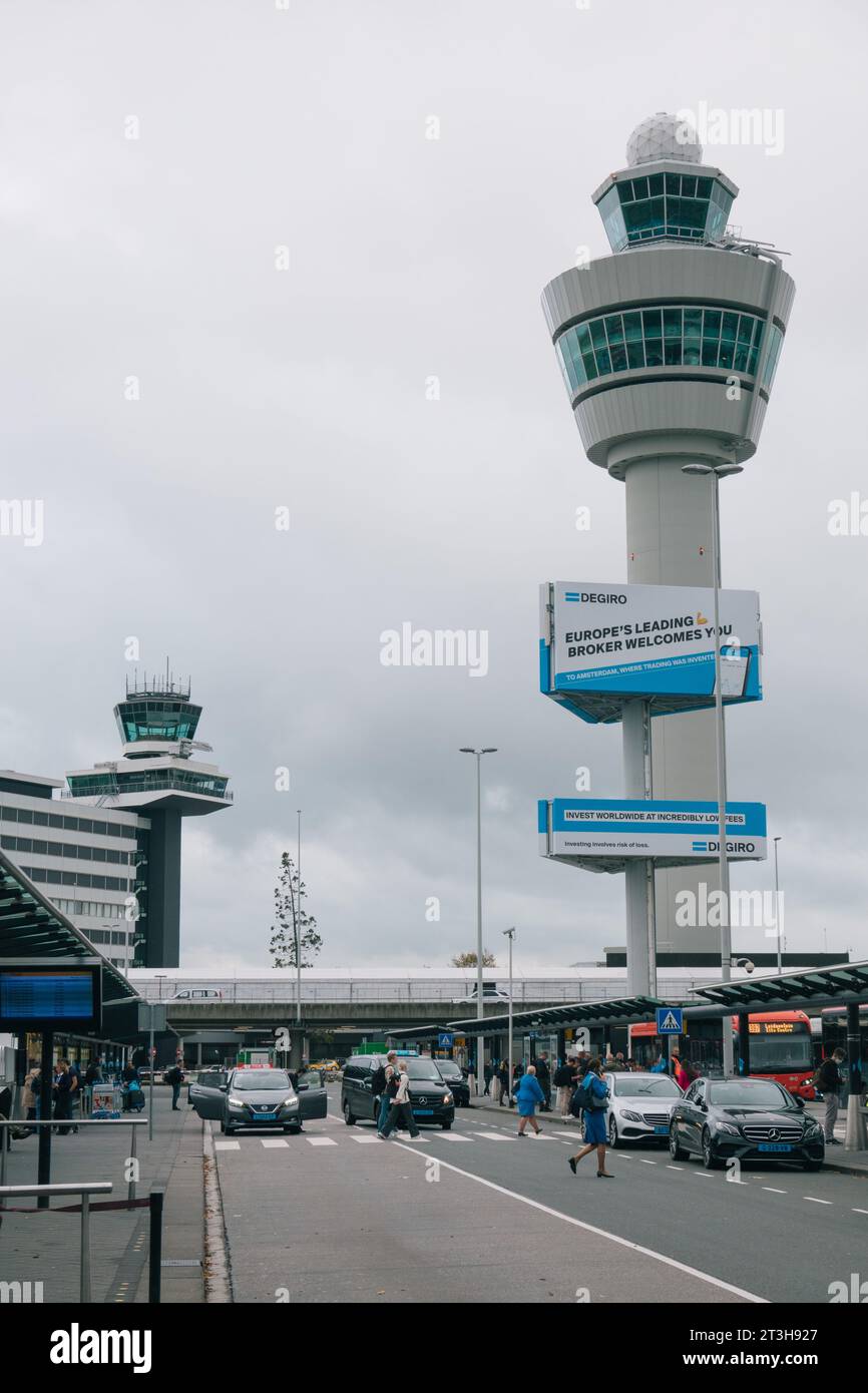 Der Kontrollturm am Flughafen Amsterdam Schiphol, von der Ankunftshalle aus gesehen, an einem bewölkten Tag. Eine DEGIRO-Anzeige ist auf einer Plakatwand zu sehen. Stockfoto