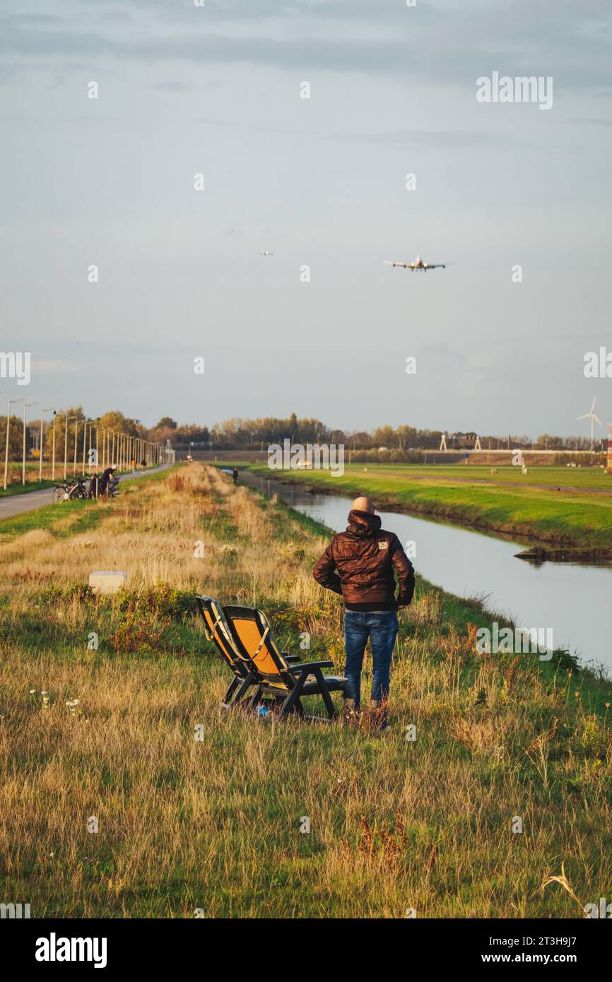 Ein Mann mit Klappstuhl beobachtet eine Landung 747 auf der Polderbaan am Flughafen Amsterdam Schiphol, Niederlande. Die Landebahn ist durch einen Kanal gesichert Stockfoto