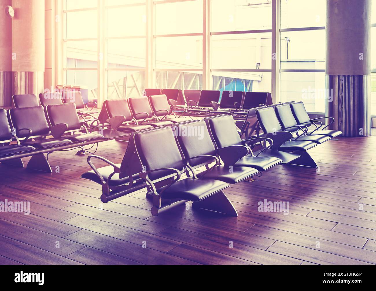 Leere Sitzplätze in einer Abflughalle des Flughafens bei Sonnenuntergang, farblich gefärbtes Bild, selektiver Fokus. Stockfoto
