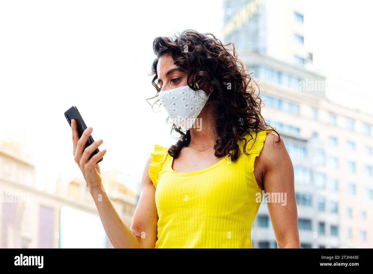 Frau mit Maske, die auf das Handy in der Stadt schaut Stockfoto