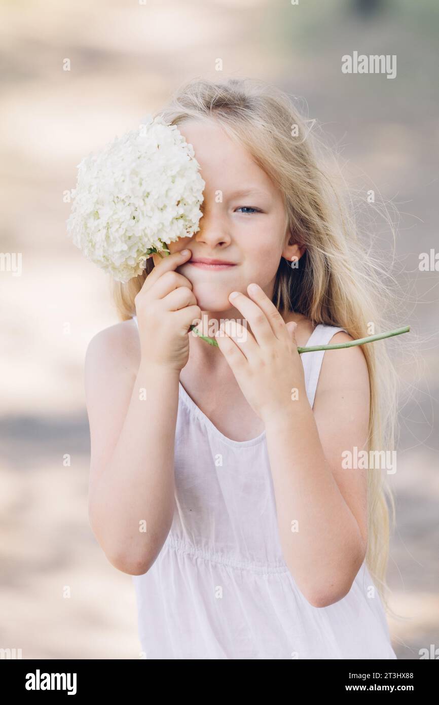 Porträt eines jungen, schönen Mädchens, das einen Teil ihres Gesichts hinter einer Hortensie versteckt und lächelt. Vertikaler Rahmen. Stockfoto