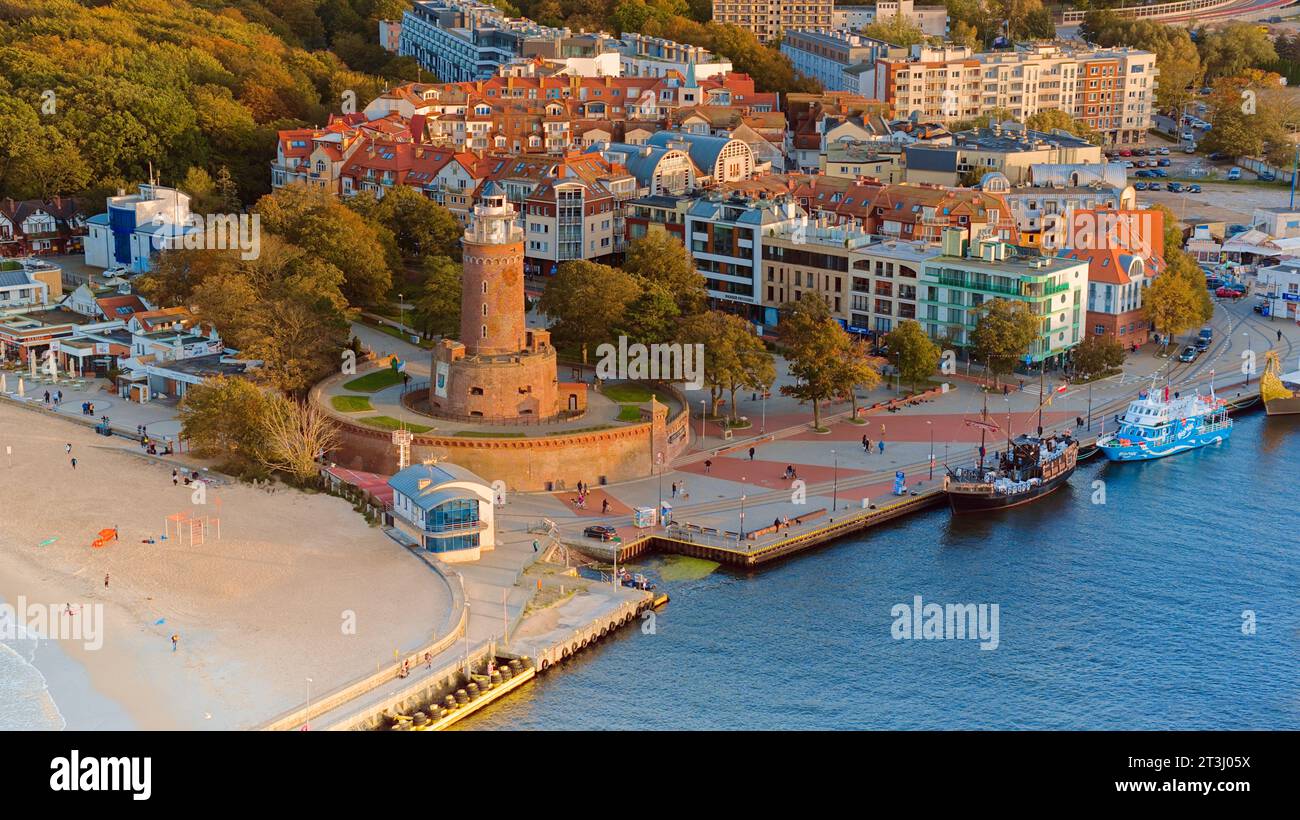 Das Drohnenfoto fängt Kołobrzeg maritimen Charme ein, mit dem berühmten Leuchtturm, dem braunen Meer, turbulenten Wellen und einem entfernten Pier. Stockfoto