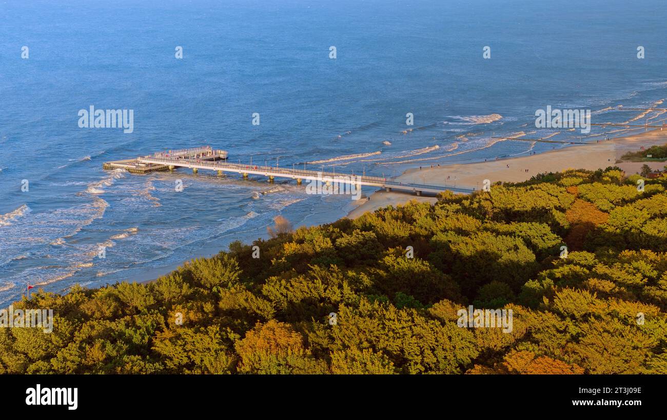 Genießen Sie die sonnenverwöhnte Ruhe am Pier von Kołobrzeg, wie auf diesem Drohnenfoto festgehalten. Der weitläufige Holzsteg erstreckt sich bis in die azurblaue Ostsee. Stockfoto