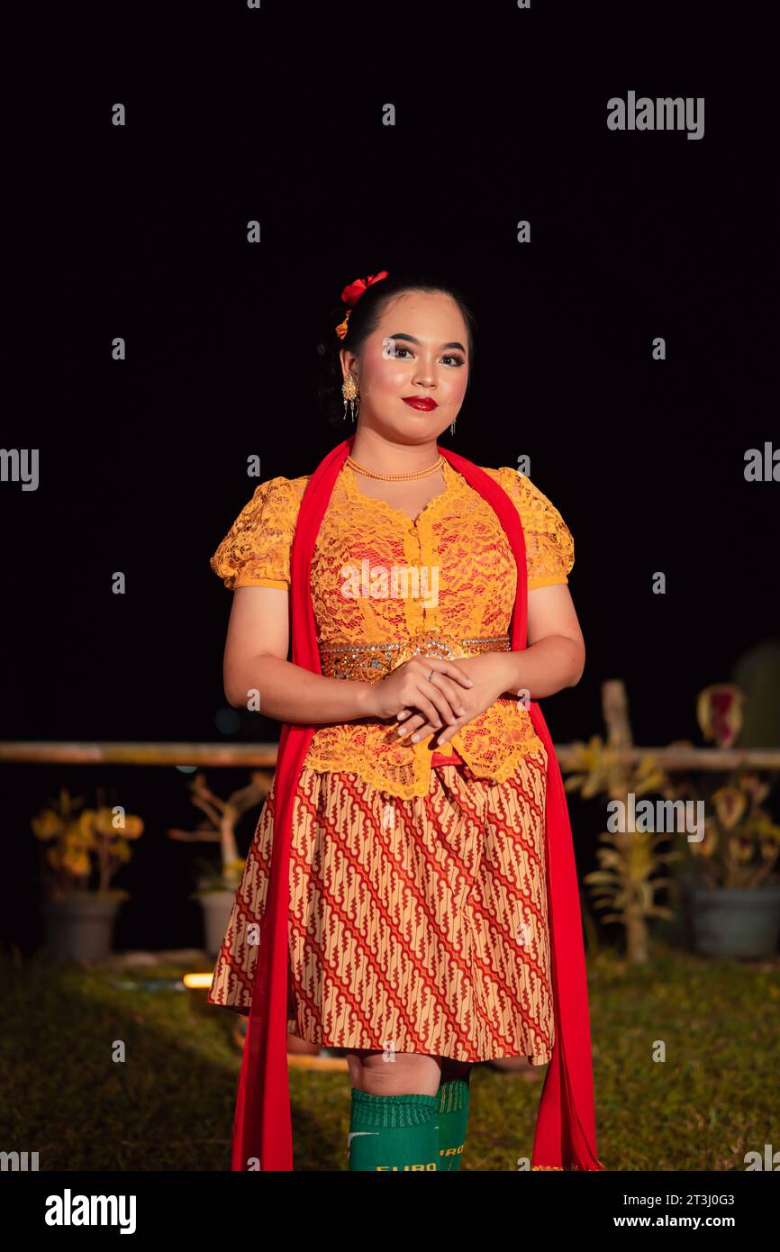 Sundanese Frau, die nach der Tanzvorstellung auf der Bühne ein kurzes Kleid und ein traditionelles gelbes Kleid mit rotem Schal und Make-up trägt Stockfoto
