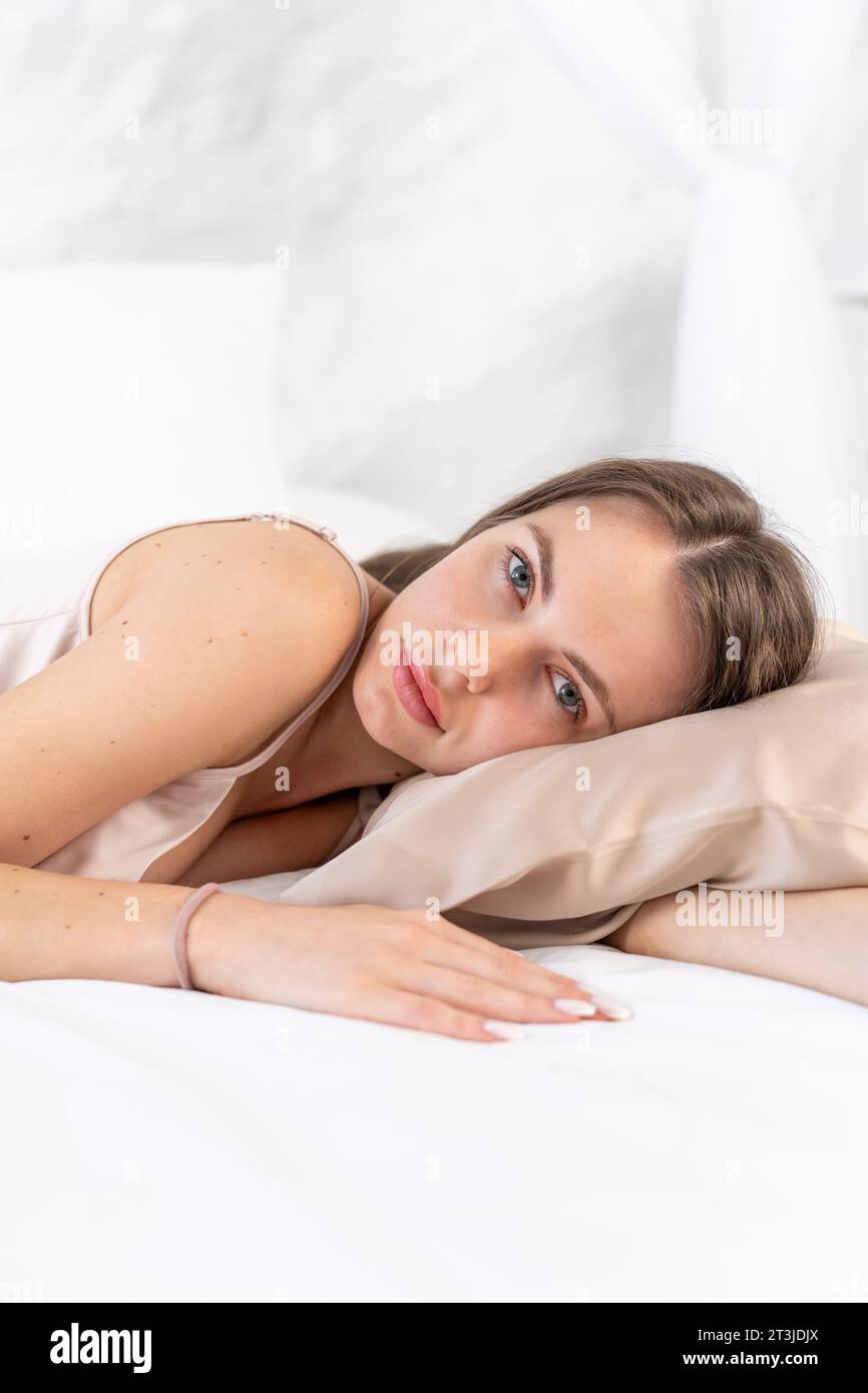 Attraktives weißes Mädchen in Seidenwäsche schläft auf einem Schönheitskissen auf einem weißen Bett im Schlafzimmer Stockfoto