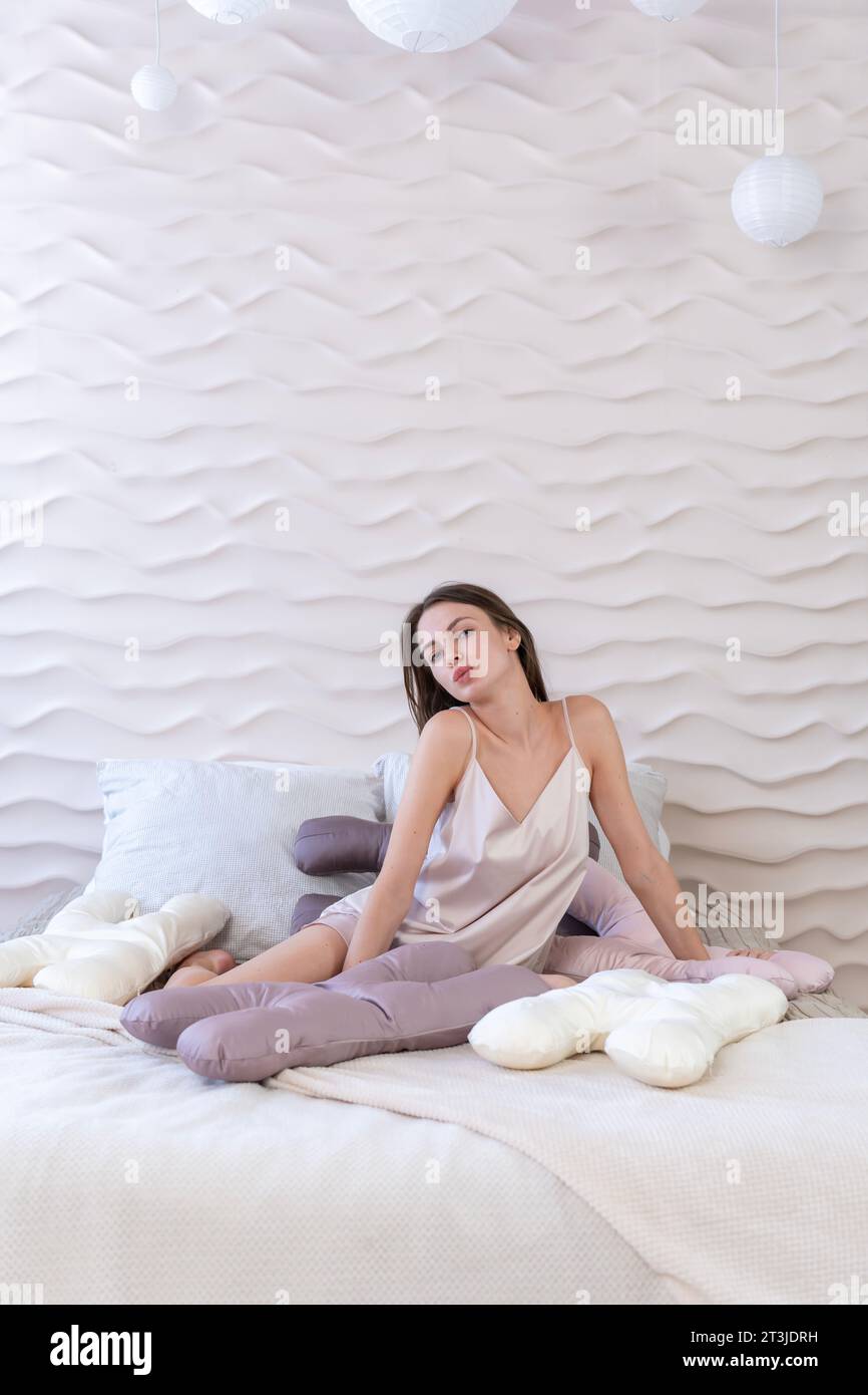 Weißes sexy Mädchen 20-25 Jahre alt mit einem Schönheitskissen in den Händen, das sich im Bett entspannt Stockfoto