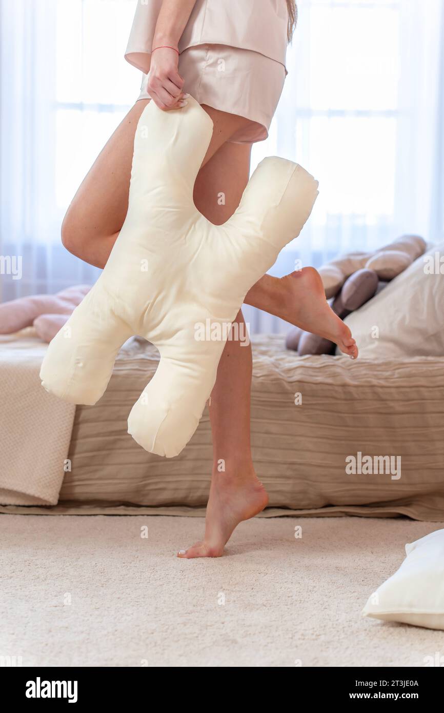 Seidenbeige Schönheitskissen vor dem Hintergrund von schlanken sexy weiblichen Beinen Nahaufnahme. Vertikales Foto Stockfoto