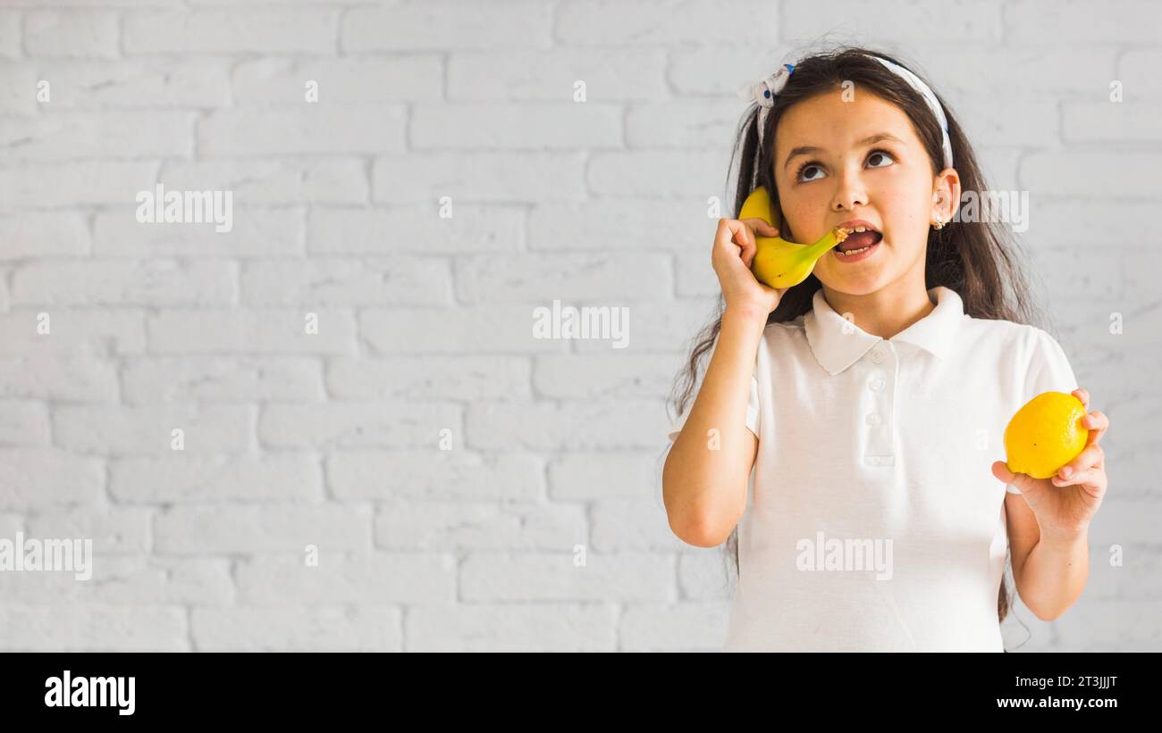 Das verrückte Mädchen hält Zitrone in der Hand und macht Spaß mit der gelben Banane Stockfoto