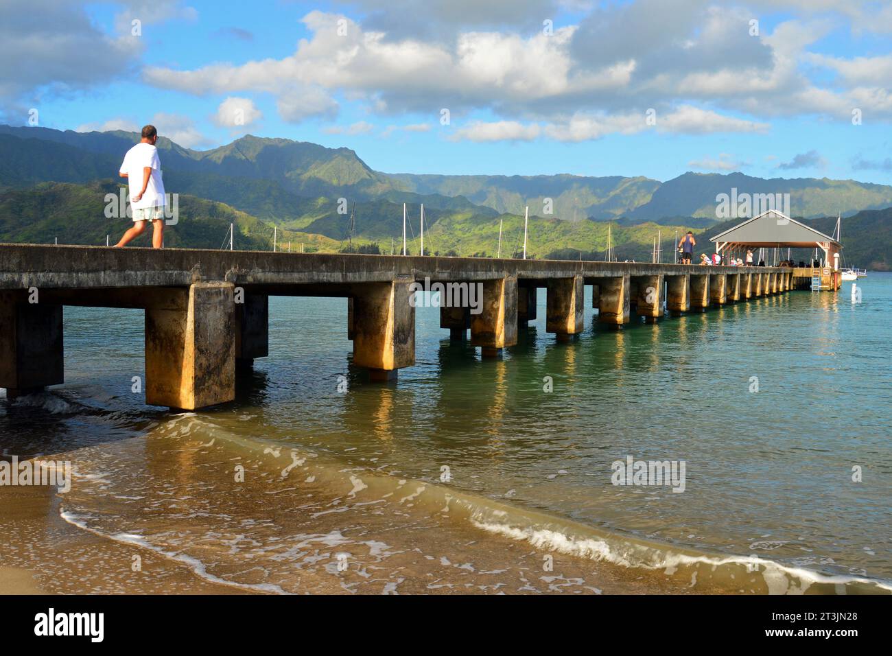Ein erwachsener Mann spaziert auf dem Pier, der sich in die Hanalei Bay auf der tropischen Insel Kauai, Hawaii, erstreckt Stockfoto
