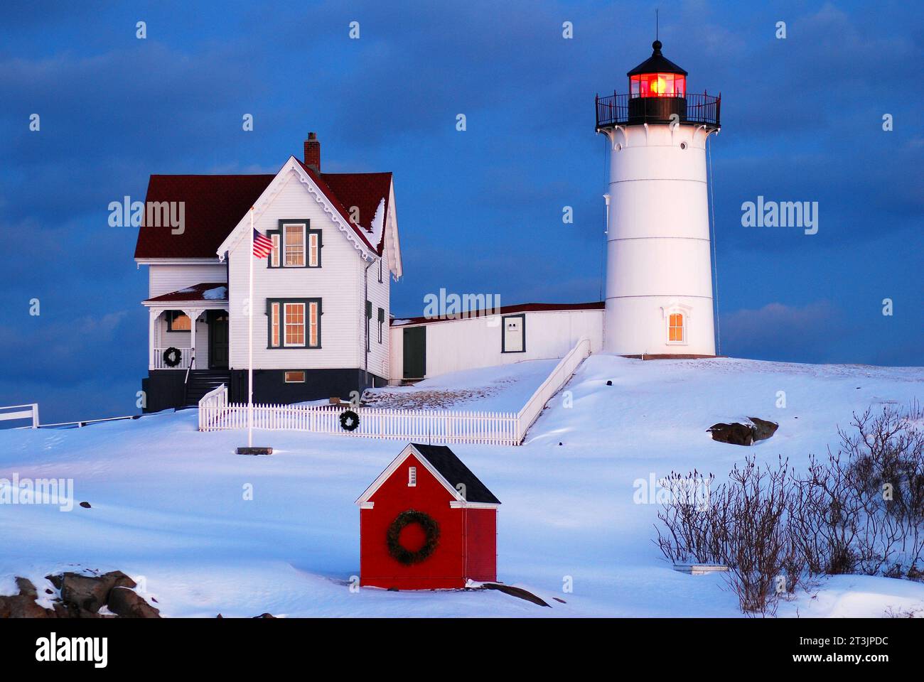 Der Nubble Lighthouse ist mit einem Weihnachtskranz an der Küste von Maine dekoriert und strahlt sein Leuchtfeuer auf einer schneebedeckten kalten Winternacht Stockfoto