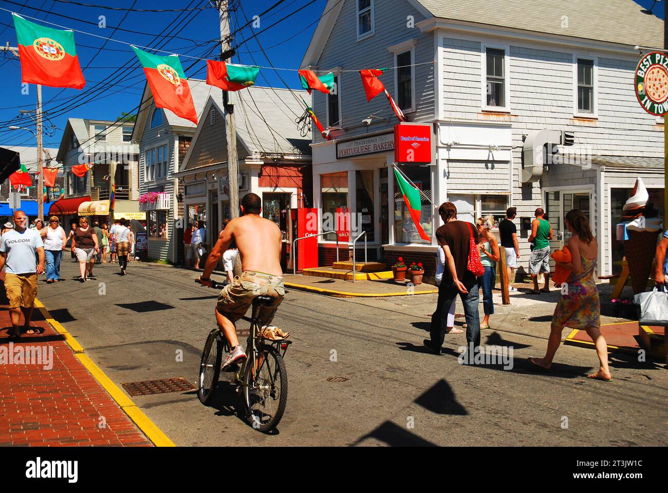 Die Leute laufen und fahren mit dem Fahrrad entlang der Commercial Street, der Hauptstraße in Provincetown, Cape Cod, mit portugiesischen Fahnen, die an den Gebäuden hängen Stockfoto