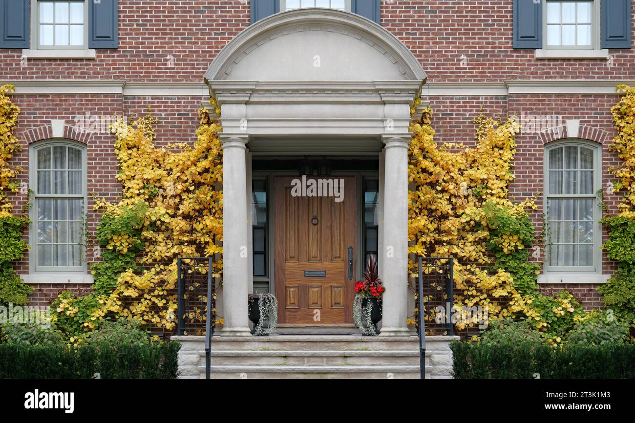 Traditionelles zweistöckiges Backsteinhaus mit eleganter Eingangstür aus Holz und goldfarbenen Weinstöcken im Herbst Stockfoto