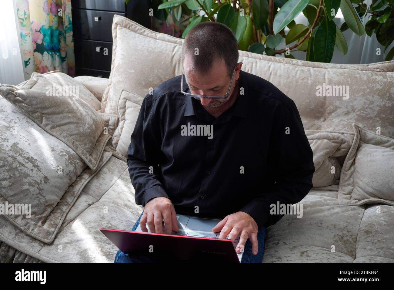 Mann sitzt auf dem Sofa und arbeitet am Laptop Stockfoto