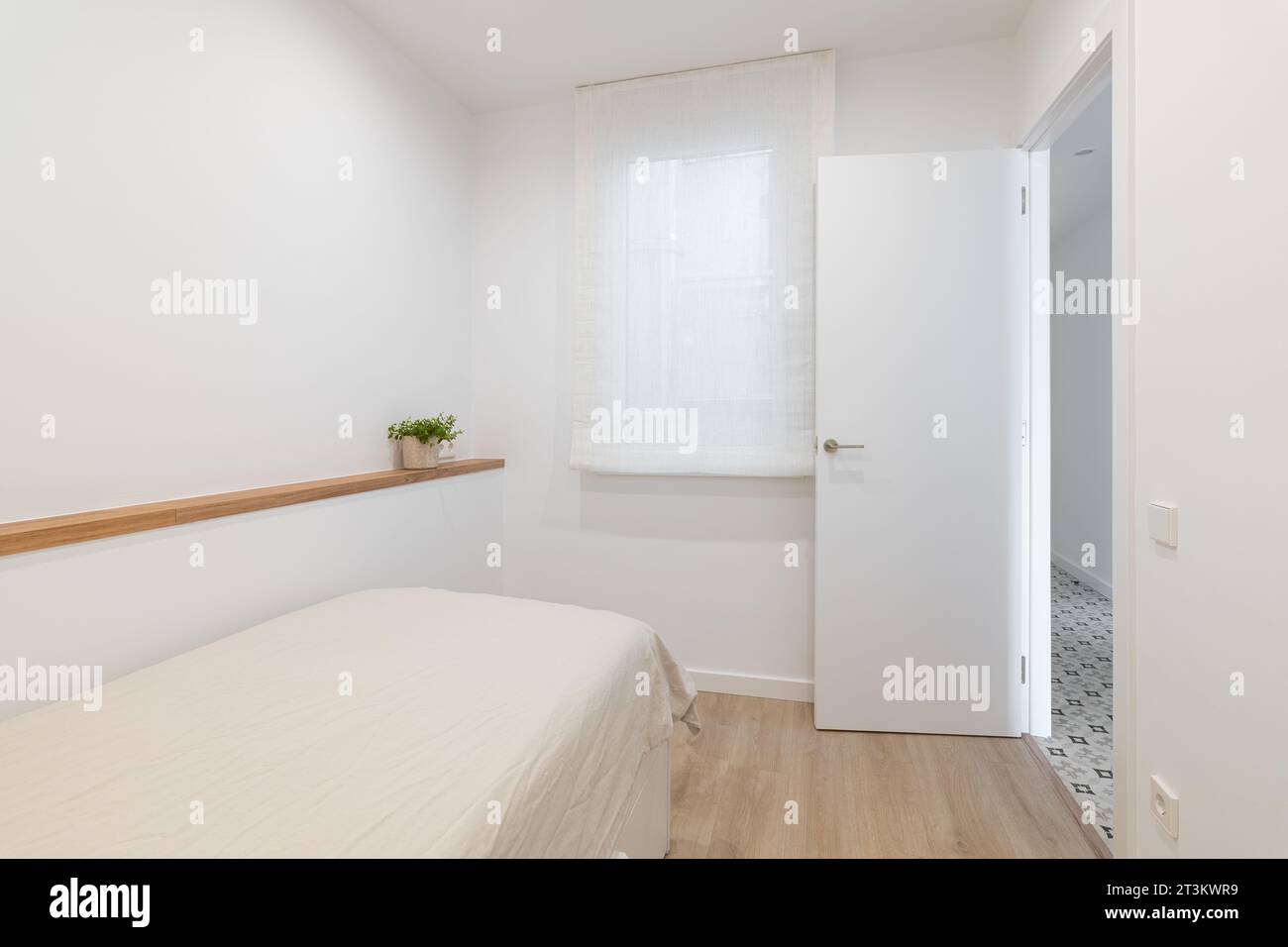 Bett mit Decke und schmalem Regal an der Wand im weißen Schlafzimmer Stockfoto