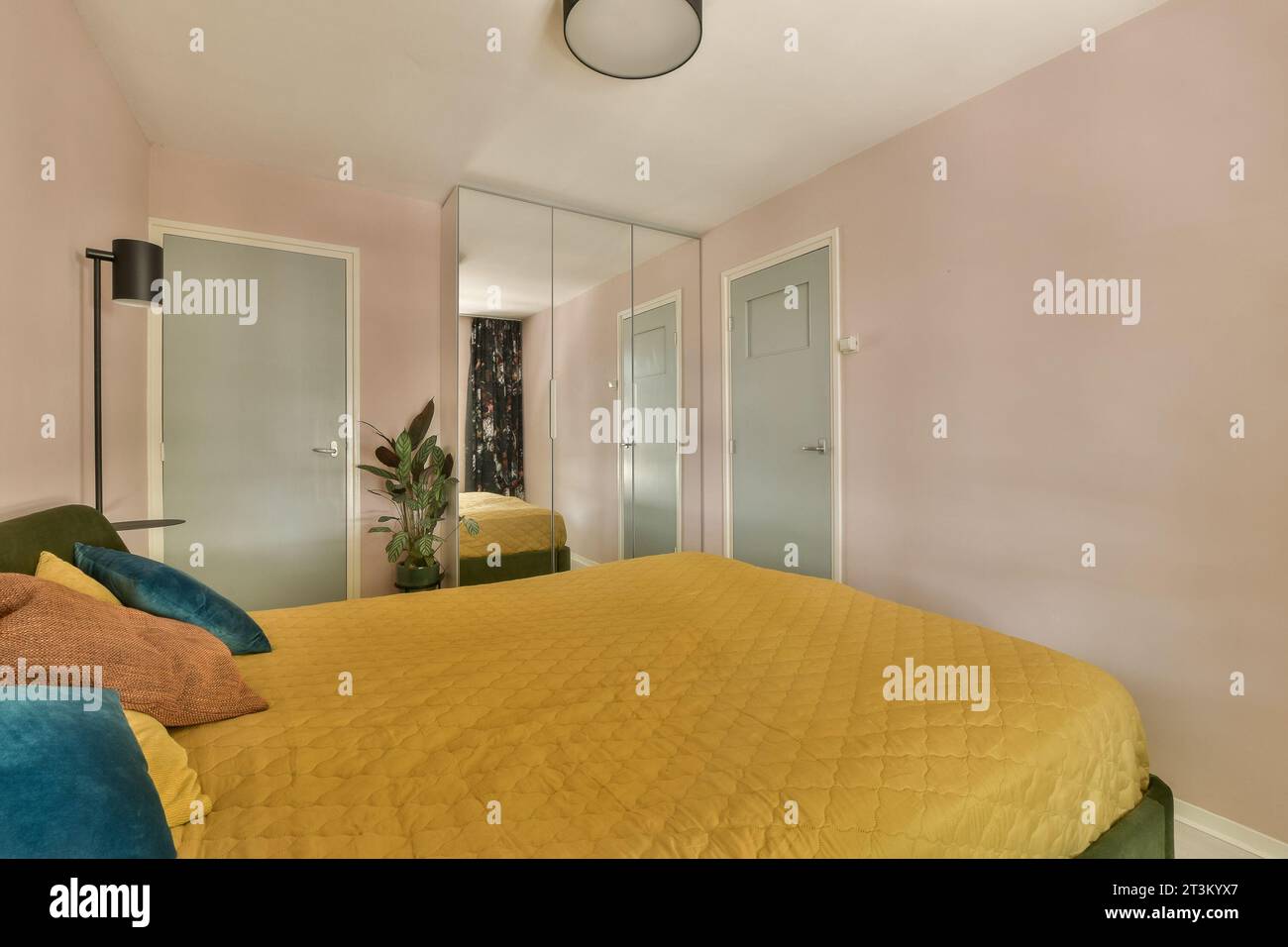 Ein Schlafzimmer mit pinkfarbenen Wänden und gelber Bettdecke in der Mitte des Zimmers ist ein Spiegel an der Wand Stockfoto